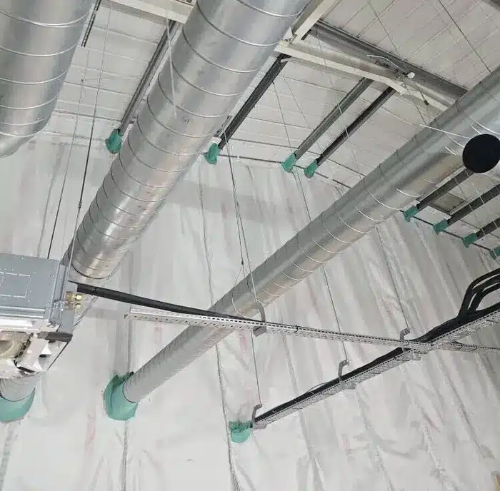 Ductwork, pipework and cable tray passing through a fire-rated ceiling with fire-stopping collars at the penetrations